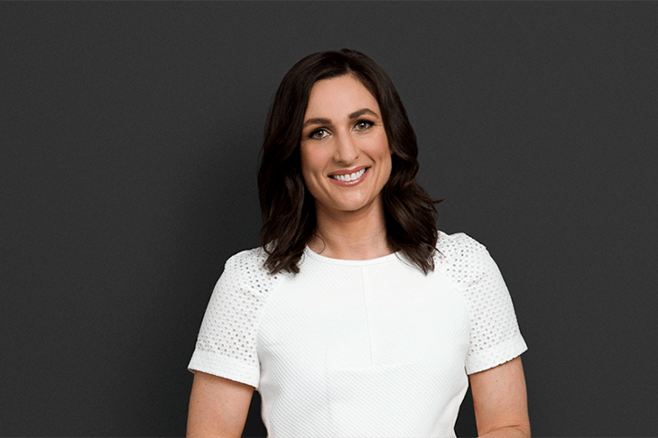 A portrait of private investigator Julia Robson, who's wearing a white t-shirt and standing in front of a grey background.